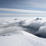 Adventure awaits with a snowy mountain peak majestically rising above a blanket of clouds, ready for exploration.