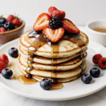 Mouthwatering pancakes topped with a medley of juicy berries and syrup, perfect for a sweet breakfast.