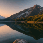 Calm waters of a mountain lake at sunrise, reflecting the vibrant colors of dawn, surrounded by towering peaks and serene wilderness.