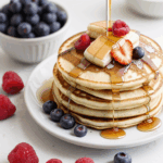 A beautiful pancake stack with syrup and berries, providing a burst of flavor and color to any breakfast table.