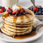 A stack of pancakes with syrup and a colorful mix of fresh berries, promising a delectable morning experience.