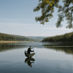 The silhouette of a man fishing at a tranquil lake during sunset.