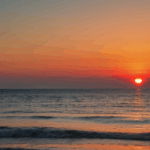 Golden hour at the ocean, with the sunset casting a warm glow over the water.