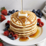 Pancakes with syrup and fresh berries, offering a delightful contrast of flavors and textures for breakfast.