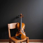 Artistic display of a violin resting on a wooden chair, exuding elegance.