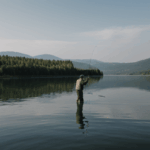A man casting his fishing rod into the serene lake, surrounded by nature's calm.
