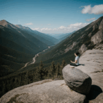 A person meditates peacefully on a mountain top with panoramic views, experiencing mindfulness and tranquility.
