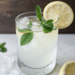 Mint garnished lemonade in a glass, chilled with ice cubes.