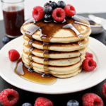 A stack of pancakes drizzled with syrup and topped with fresh berries, offering a colorful and delicious breakfast treat.