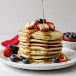 A tempting stack of pancakes adorned with syrup and a colorful variety of berries, perfect for brunch gatherings.
