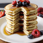 A stack of rich, syrup-covered pancakes topped with juicy berries, offering a delightful breakfast treat.