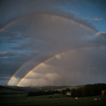 A vibrant rainbow stretches over a tranquil countryside landscape, creating a serene and colorful scene.