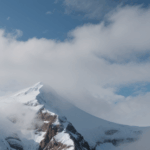 Serene landscape of a snowy mountain peak against a backdrop of clouds, offering a peaceful escape into nature.