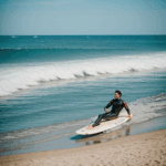 A surfer relaxing on the beach, enjoying the sun and waves in a serene coastal setting.