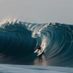 A surfer expertly riding a colossal wave in the ocean, showcasing incredible balance and skill.