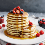 Golden pancakes with a generous drizzle of syrup and an artistic arrangement of fresh berries, capturing the essence of a sweet breakfast.