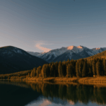 The calm waters of a mountain lake mirror the soft colors of dawn, with majestic mountains in the background, offering a peaceful and captivating landscape.