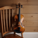 A classic violin elegantly rests on a wooden chair, showcasing its timeless beauty.